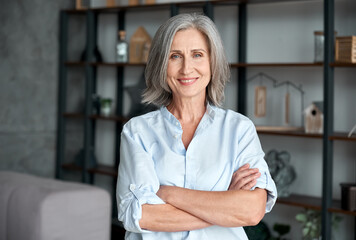 smiling confident stylish mature middle aged woman standing at home office. old senior businesswoman