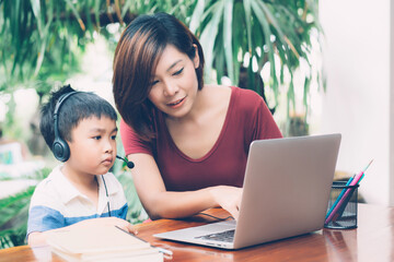 Wall Mural - Young asian mother and son using laptop computer for study and learning together at home, boy wearing headphone for e-learning with distancing, teacher or mom support child, education concept.