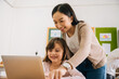 © twinsterphoto - Young Asian teacher watching Caucasian school girl using computer in school classroom, digital native, technology, learning, guidance, education. Female instructor and student smiling.