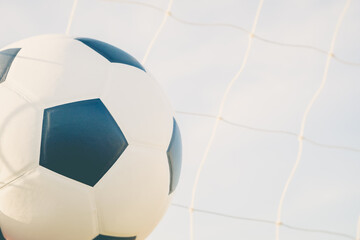 View of classic leather soccer ball in goal net on blue sky nature background. Traditional black and white football equipment to play competitive game sport tournament concept.