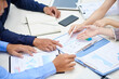 © DragonImages - Hands of entrepreneurs pointing at chart in financial report on table and discussing company development