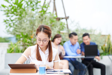 Poster - Smart serious Vietnamese female university student listening to music in earbuds when sitting at outdoor cafe table and working on project