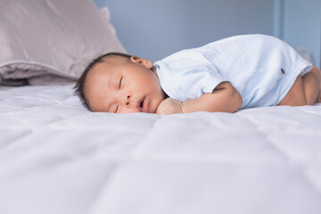 Shot of the little Asian baby boy is sleeping on the bed at home. Nursery for young children. Breastfeeding or early childhood development concept