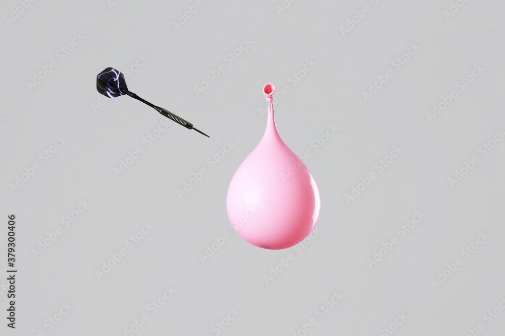 Throwing of dart in balloon with water on grey background