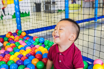 Happy little Asian baby boy laughing and playing colorful plastic balls at indoor playground center. Copy space