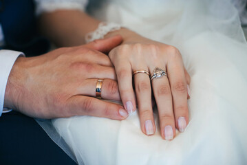 hands of bride and groom with gold wedding rings on white dress background