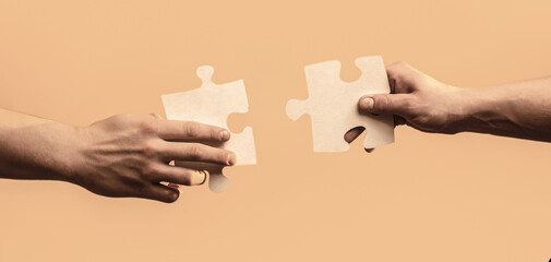 Two hands trying to connect couple puzzle with yellow background. Closeup hands of man connecting jigsaw puzzle