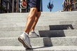 © Vlad - Young man exercising outside. Cut view of strong powerful legs and feet in sneakers. Muscled calf. Man walking up on steps at urban building. One more step. Summertime outside.