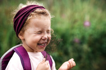 portrait of small toddler girl outdoors in summer nature, tickling face with grass.