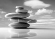 canvas print picture - Five stones forming a balanced stack on top of a polished table top and clouds in background. Black and white image
