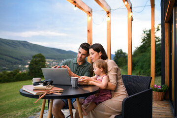 Family with small daughter using laptop outdoors, weekend away in container house in countryside.