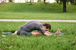 © OneWellStudio - Young athletic man in sportswear doing yoga in the park. Practice Janu Sirshasana asana head to knee pose outdoors. People exercising stretching on green grass with yoga mat.