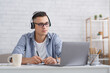 Modern student or pupil studies at home. Serious guy with glasses and headphones makes notes in notebook and looks at laptop, listening lecture