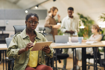 Wall Mural - portrait of young serious african-american woman looking at camera while using digital tablet sittin
