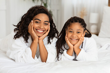 Wall Mural - portrait of happy black mother and daughter in bathrobes posing on bed