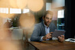 © mavoimages - Smiling young businessman using a tablet at his office desk