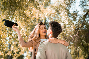 excited woman with hat hugging boyfriend in autumnal park