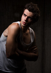 Sexy male model posing in white underwear in dark shadow background with  emotional face on shadows. Closeup portrait of strong handsome man.