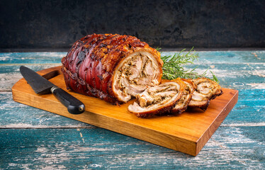 Traditional Italian Porchetta arrotolata pork meat sliced and as piece with herbs offered as close-up on a modern design wooden board