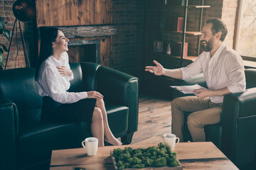 Photo of two business people share corporate news drink hot coffee mug beverage break chatting friendly interview asking questions formalwear clothes sit couch modern office indoors