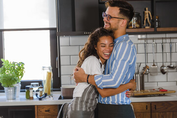 Young cheerful multi ethnic couple preparing pasta together at their modern kitchen