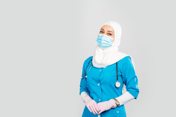 Wall Mural -  friendly Muslim doctor or nurse wearing hijab and medical face mask and gloves on a gray background.