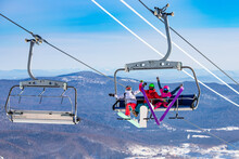 Fun team of friends skier and snowboarders up ski lift on blue sky background
