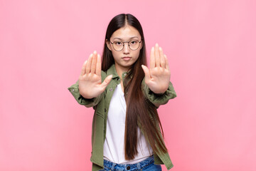 Wall Mural - asian young woman looking serious, unhappy, angry and displeased forbidding entry or saying stop with both open palms