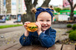 Young happy little girl eat burger in outdoors cafe