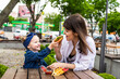 © dianagrytsku - Cheerful cute little girl sitting with her mother with burger and fries on table in a cafe