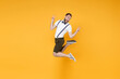 © ViDi Studio - Full length side view portrait of excited young bearded man 20s wearing white shirt suspender shorts posing jumping showing victory sign looking camera isolated on yellow color wall background studio.