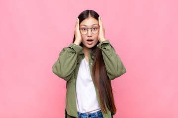 Wall Mural - asian young woman looking unpleasantly shocked, scared or worried, mouth wide open and covering both ears with hands