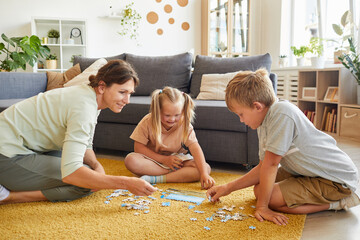 Full length portrait of loving family with special needs child playing board games and puzzles while sitting on floor at home, copy space