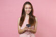 © ViDi Studio - Smiling beautiful attractive young brunette woman 20s wearing pink summer dotted dress posing using mobile cell phone typing sms message isolated on pastel pink color wall background studio portrait.