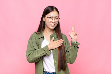 Wall Mural - asian young woman looking happy, confident and trustworthy, smiling and showing victory sign, with a positive attitude