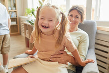 Portrait Of Cute Girl With Down Syndrome Laughing Happily While Playing With Mother At Home