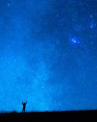 person raising arms under the blue starry sky at night. silhouette of a person observing the immensi