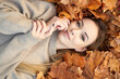 © Kiryl Lis - Pretty young girl with charming smile liying in the autumn leaves and enjoying it, holding face and smiling. Autumn portrait in the autumn park. Top view.