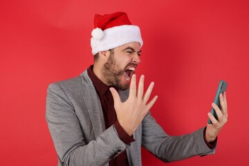 Angry Young caucasian businessman wearing casual clothes standing over isolated red background screaming on the phone, having an argument with an employee. Troubles at work.