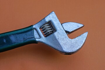 one gray iron adjustable wrench with a handle in green plastic on a brown table