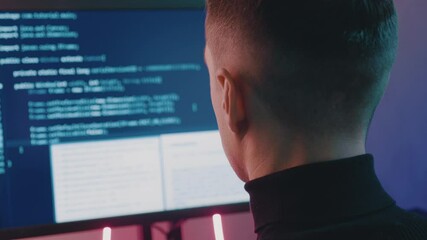 Rear view of software developer working on project. Portrait of man hacker working on computer at night in neon lights.