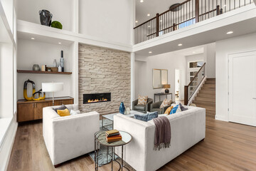 Beautiful living room interior in new luxury home with large stone fireplace surround, hardwood floors, and tall ceiling.