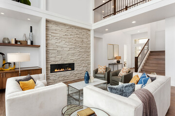 Beautiful living room interior in new luxury home with large stone fireplace surround, hardwood floors, and tall ceilings.