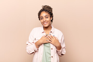 young afro woman feeling romantic, happy and in love, smiling cheerfully and holding hands close to heart