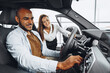 © fotofabrika - Young attractive woman salesperson in car showroom showing a car to her male client