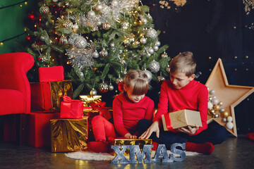 Cute little girl in a red sweater. Brother and sister sitting by the christmas gifts