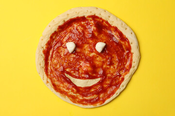 Pizza dough with sauce and smile on yellow background