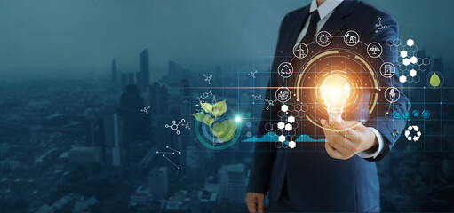 Wall Mural - businessman holding light bulb against nature on city background with icons energy sources for renew