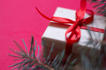 Christmas gift from a box tied with a red ribbon on a red background with a spruce, green branch. The view from the top. Space for text. A soft picture