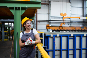 Portrait of smiling female factory worker standing in industrial production hall.